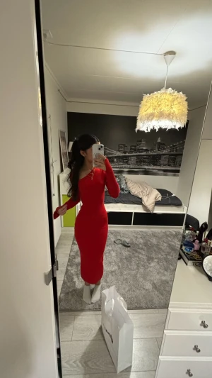 Röd ribbad långklänning oneshoulder - Säljer en snygg röd långklänning med ribbad struktur och oneshoulder-design. Klänningen är figurnära och har långa ärmar, perfekt för dig som vill sticka ut med en trendig och stilren look.