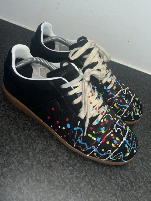 Maison Margiela sneakers med färgstänk - Ett par sköna Gats sneakers i svart skinn med unika färgstänk. Perfekt för dig som vill sticka ut med ett konstnärligt och edgy uttryck. Skorna är i nyskick, 9/10, och priset är satt därefter då kvitto o box saknas. Hör gärna av dig om du undrar över något!!! ‼️