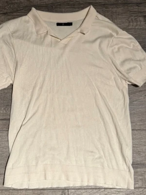 Vit piké t-shirt från Åhléns  - Snygg vit/beige piké t-shirt från Åhlens med klassisk krage och korta ärmar. Tillverkad i mjuk bomull som känns skön mot huden. Perfekt till jeans eller shorts för en clean och enkel stil.