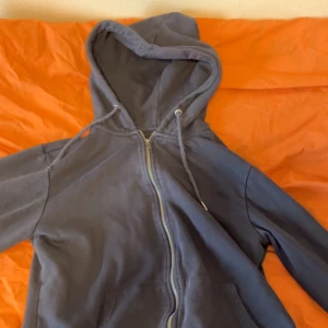 Mörkblå zip hoodie med huva lager 157 - Säljer en enkel och stilren mörkblå hoodie med dragkedja framtill och justerbar huva med snören. Hoodien har två fickor på magen och är gjord i mjukt sweatshirtmaterial. Perfekt för en avslappnad och bekväm stil.