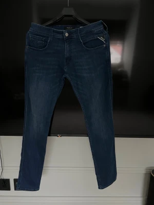 Blå Replay jeans med dragkedjedetalj - Snygga blå jeans från Replay med klassisk femficksdesign och en extra dragkedjedetalj på ena fickan framtill. Jeansen har en smal passform och är tillverkade i stretchigt denim för extra komfort. Aldrig använda. Stl 29/32