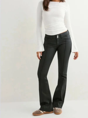 Coated Low Waist Stitch Jeans - Snygga svarta jeans med bootcut-modell.  Jeansen har dubbla knappar i midjan, markerade sömmar framtill och klassiska fem. Snygg design på fickorna bak . Byxorna har prislappen kvar . POSTAR SNABBT (lånade bilder från Nellys hemsida )