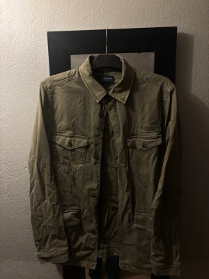 Beige overshirt från Lexington - Stilren beige overshirt från Lexington med klassisk krage och fyra fickor framtill. Skjortjackan har knappar längs hela framsidan och är tillverkad i bomull. Perfekt att slänga över en hoodie eller t-shirt för en avslappnad look.
