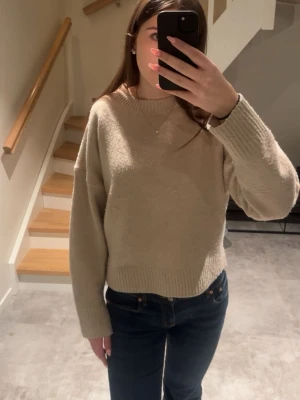 Beige stickad tröja  - Mysig beige stickad tröja med rund halsringning och långa ärmar. Tröjan har en avslappnad passform och ribbstickade muddar vid ärmslut och nederkant. 