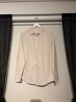 Ljusbeige skjorta i linnen - Stilren ljusbeige skjorta med klassisk krage och knäppning framtill. Skjortan har lång ärm. Perfekt för en clean och enkel look.