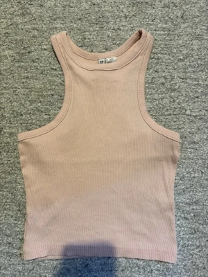Dam ribbad tank top   - Säljer en beige/rosa ribbad tank top från H&M. Toppen är ärmlös med rund halsringning och croppad passform. Perfekt att styla till jeans eller kjol för en enkel och trendig look.
