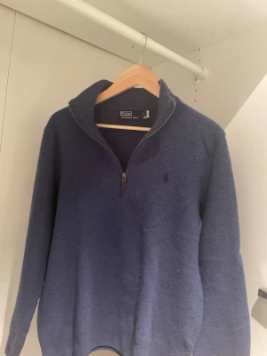 Marinblå stickad tröja Polo Ralph Lauren - Säljer en marinblå stickad tröja från Polo Ralph Lauren med half zip och hög krage. Klassisk broderad logga på bröstet och ribbade muddar. Perfekt för kyliga dagar och enkel att matcha med jeans eller chinos. Finns noppor. 