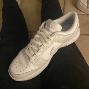 Nike Dunk Low photon dust - Nike Dunk Low photon dust med klassisk siluett och lågt skaft. Skon har grå sula, perforerad tåbox och vita snören. Swoosh-logga på sidan och Nike-broderi på hälen. Perfekt clean look för dig som gillar minimalistisk stil. Pris 5500kr på merch sweden kom med bud kollar intresse