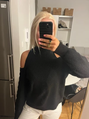 Svart stickad offshoulder-tröja Y.A.S - Säljer en svart stickad tröja från Y.A.S med offshoulder-design och hög hals. Tröjan har lång ärm och en snygg struktur i materialet som ger en cool vibe. Perfekt att styla med jeans eller kjol för en trendig look.