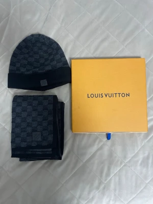 Mörkgrå halsduk från Louis Vuitton - Säljer en snygg mörkgrå halsduk från Louis Vuitton med klassiskt rutmönster och diskret logotyp. Halsduken är stickad i mjukt material och har en exklusiv känsla. Perfekt accessoar för att lyfta din outfit och hålla dig varm under kyliga dagar.