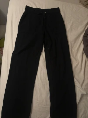 Svarta mjukisbyxor med snörning - Svarta mjukisbyxor med avslappnad passform och resår i midjan samt snörning. Byxorna har praktiska fickor på sidorna och är perfekta för chill dagar. Tillverkade i mjukt material som känns skönt mot huden.