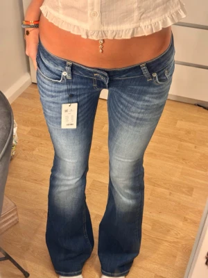 Blå bootcut jeans låg midja - Snygga blå bootcut jeans med låg midja och slitna detaljer. Jeansen har klassisk femficksdesign och en tvättad look som ger en cool vibe. Perfekta för dig som gillar en avslappnad men trendig stil.