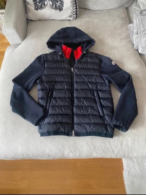 Moncler Cardigan  - Snygg navy cardigan från Moncler i modellen Maglia. Riktigt stilren och har huva, dragkedja framtill, logga på ärmen och röd detalj på insidan av kragen. Storleken är klass 1. Står storlek M men monclers storlekar är något små i storleken så skulle säga att den passar S bättre. Nypris 11-13 000 kr. Postar inom 24h📦 Köp mer än ett plagg för 10% rabatt!🤝