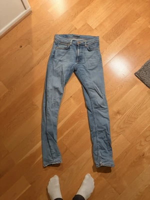 Ljusblå  jeans från Nudie - Säljer ett par ljusblå  jeans från Nudie med klassiska fem fickor och orange sömmar. Lean Dean 29:34
