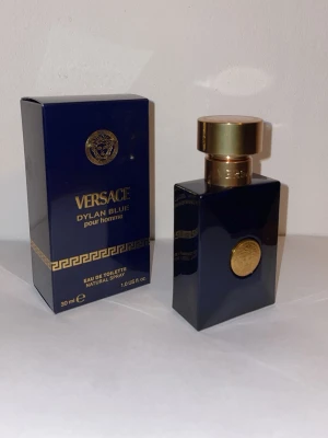 Versace Dylan Blue pour homme 30 ml - Versace Dylan Blue pour homme är en elegant parfym i en mörkblå, fyrkantig glasflaska med gulddetaljer och Versaces ikoniska Medusa-logga. Innehåller deremot ingen parfym och är en prydnad. Flaskan rymmer 30 ml Eau de Toilette och har en lyxig känsla med sin djupa blå färg och guldiga lock.