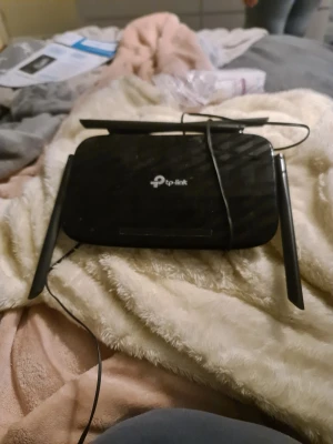 Svart TP-Link router med antenner - Trådlös router från TP-Link i svart plast med tre externa antenner för bättre räckvidd. Perfekt för att förbättra wifi-täckningen hemma. Kompakt och stilren design, enkel att placera i hemmet.