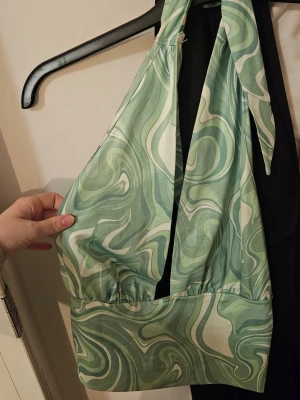 Grön swirl mönstrad halterneck topp - Säljer en snygg halterneck topp med grönt och vitt swirl-mönster. Toppen har breda knytband i nacken och är ärmlös med croppad passform. Omsydd av mig.