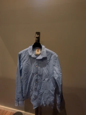 Ljusblå skjorta från Strömberg - Snygg ljusblå skjorta från Strömberg med diskret prickigt mönster och klassisk krage. Skjortan har knappar framtill och är långärmad. Perfekt för dig som gillar stilrena plagg med en twist.