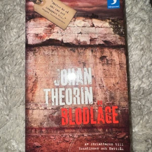 Blodläge av Johan Theorin - En spännande pocketbok med titeln 'Blodläge' av Johan Theorin. Omslaget har en dramatisk rödbrun och beige färgskala med naturmotiv. Perfekt för dig som gillar deckare och thrillers med mystik och spänning.