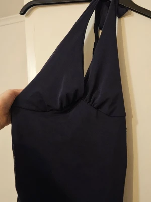 Mörkblå halterneck top - Snygg mörkblå top med halterneck och djup urringning. Topen har en enkel, stilren design och knyts i nacken. Materialet känns stretchigt och följsamt, perfekt för sommaren