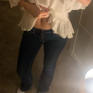 Mörkblå bootcut jeans från Gina young - Säljer ett par mörkblå jeans med bootcut-modell och vita kontrastsömmar. Byxorna har låg midja och snygga fickdetaljer med knapp bak. Klassisk jeanslook som passar till det mesta och ger en schysst siluett.