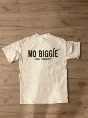 Oversized vit t-shirt från NO BIGGIE - Säljer en clean oversized vit t-shirt från NO BIGGIE i storlek XS. T-shirten har tryck med loggan på bröstet och stort print på ryggen. Klassisk passform med rund hals och korta ärmar. Perfekt till jeans eller shorts för en chill look. Xs passar ungefär S/M om man inte vill att den ska sitta oversize