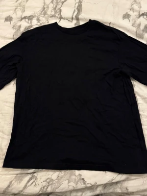 Svart långärmad t-shirt från lager 157 - En basic svart långärmad t-shirt från lager 157 i 100% bomull. Klassisk rund halsringning och enkel design som funkar till allt. Perfekt för dig som gillar stilrena plagg och vill ha något bekvämt i garderoben.