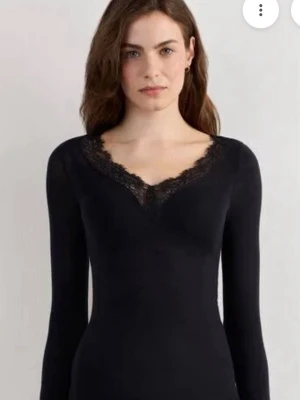 Svart långärmad topp med spets - Snygg svart långärmad topp med v-ringning och dekorativ spets runt halsen. Toppens stilrena design gör den enkel att matcha med olika outfits. Perfekt för dig som gillar en feminin touch på din look.