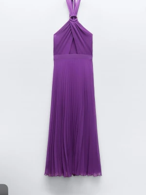 Lång lila plisserad klänning - Säljer en långklänning i en snygg lila färg med plisserad design. Klänningen har ett luftigt fall och är tillverkad i ett lätt, syntetiskt material. Perfekt för dig som vill sticka ut med en färgstark look. Dragkedja kan kärva och trådarna har släppt lite längst ned vid den.
