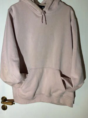 Ljusrosa hoodie från H&M - En enkel och stilren ljusrosa hoodie från H&M med huva och dragsko. Hoodien har en stor magficka och ribbade muddar vid ärmslut och nederkant. Tillverkad i mjuk bomullsblandning som känns skön mot huden. Perfekt för en avslappnad look.