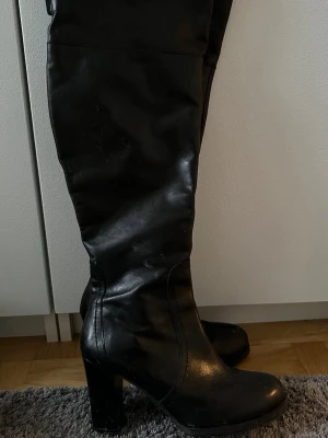 Svarta höga stövlar med klack - Snygga svarta stövlar i skinnimitation med hög klack och rund tå. Klassisk design som går upp till knäna. Perfekta att matcha med både jeans och kjol eller klänning🖤Strl. 40 men passar mig som har 39 också