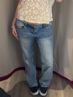  ljusblå jeans low waist - Ljusblå  jeans med låg midja och rak passform. Klassisk femficksmodell i bomull med knappgylf och subtilt slitna detaljer. Perfekta för en avslappnad och trendig look.