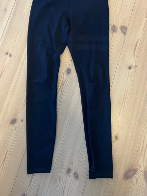 Mörkblå tights från Stronger - Snygga mörkblå träningstights från Stronger med hög midja och diskret logga framtill. Tillverkade i stretchigt funktionsmaterial som passar perfekt till gymmet eller löprundan. Tight passform och långa ben ger en sportig look.