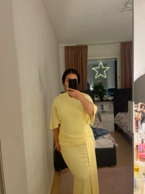 Ljusgul långklänning med öppen rygg - Säljer en ljusgul långklänning med snygg öppen rygg och korta vida ärmar. Klänningen har en draperad detalj i midjan och är figurnära med en elegant siluett. Perfekt för dig som vill sticka ut!❤️