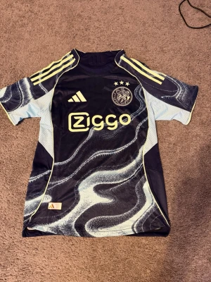 Ajax x Adidas matchtröja blå mönstrad - Snygg Ajax matchtröja från Adidas i mörkblått med ljusblå och vita vågmönster. Tröjan har korta ärmar, gula detaljer och Ziggo-logga på bröstet. Ajax klubbmärke och Adidas-logga framtill. Perfekt för fotboll och träning. Frågor? Kontakta mig✅Allt gott, mvh Noah.PS KÖP INTE MED INSTABOX TACK🙏