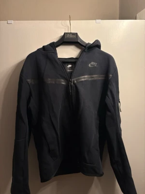 Nike Tech Fleece Full-Zip Hoodie - Black - Size S - Selling this classic Nike Tech Fleece hoodie in black. This is the essential streetwear staple known for its lightweight warmth and sleek, technical look.  Condition: Excellent condition, sparingly used. The fabric is still crisp and the zippers work perfectly.  Size: Small (S).  Details: Features the iconic chevron design on the chest and the signature vertical zip pocket on the sleeve.  Fabric: Authentic Tech Fleece material—soft, breathable, and holds its shape well.  The ziper is a bit broke