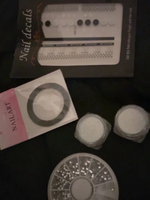 Nageldekorationer och nail art kit - Säljer ett kit med nageldekorationer: nail decals i svart och vitt med olika mönster, en rulle svart nail art tejp, två burkar med vitt glitter och ett hjul med silvriga rhinestones i olika former. Perfekt för att skapa unika och kreativa nageldesigner.
