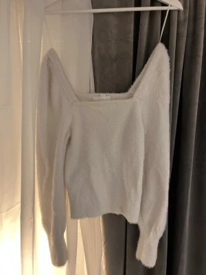 Vit fluffig stickad tröja H&M - Supersöt vit stickad tröja från H&M med fluffig känsla och fyrkantig ringning. Tröjan har långa ärmar och sitter snyggt med en lite croppad passform. Perfekt till både jeans och kjol för en trendig look.