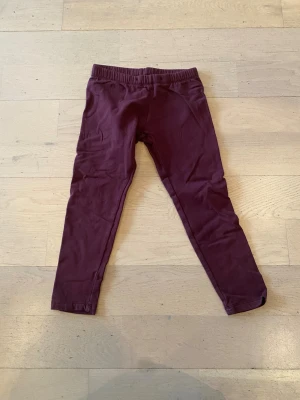 Mörklila leggings från Lindex Kids - Snygga mörklila leggings från Lindex Kids i storlek 116. De har en elastisk midja och är gjorda i mjukt bomullsmaterial som är skönt mot huden. Perfekta för chill dagar eller när du vill ha något bekvämt på dig.
