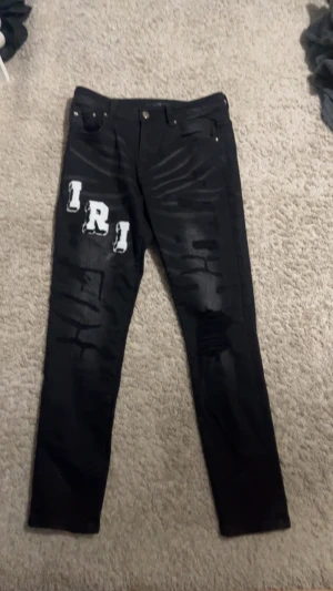 Svarta  jeans från Amiri - Svarta jeans från Amiri. Framsidan har vita bokstäver 'IRI' och baksidan 'AM' i graffiti-stil. Tillverkade i 100% bomull med ribbade detaljer i bomull och kashmir. Snygg streetwear-vibe och unika detaljer.