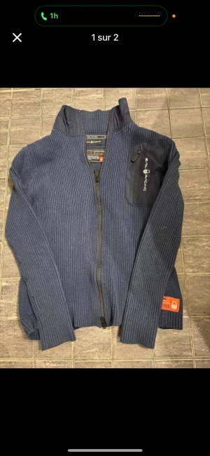 Sail racing kofta - Säljer en blå stickad jacka från Sail Racing, modell Antarctica Expedition. Jackan har ribbad struktur, hel dragkedja framtill och en praktisk bröstficka med dragkedja och logga. Perfekt för dig som gillar sportig och stilren look.