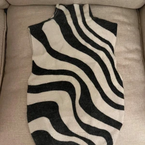 Stickad zebramönstrad väst - Snygg stickad väst med zebramönster i svart och beige. Hög krage och ärmlös design, perfekt att styla över en skjorta eller t-shirt. Västen har en mjuk och följsam passform som ger en trendig look.