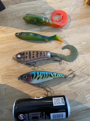 Fiskedrag blandat set - Säljer ett set med fyra fiskedrag i olika färger och former, perfekt för gädd- och abborrfiske. Drag i plast och metall med skarpa krokar, några med synligt slitage men fullt funktionella. Se bilder för storlek (Pepsi-burk som referens). Bra för både nybörjare och erfarna fiskare. Allt från 50-120g kan köpas styck pris för 150krst eller alla för 500