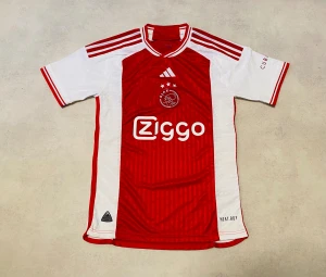 Ajax 23/24 hemmatröja Adidas S - Ajax Amsterdam 23/24 hemmatröja från Adidas i slim fit. Röd och vit med randiga detaljer, klubbmärke och Ziggo sponsortryck på bröstet. Kortärmad med klassisk krage och HEAT.RDY-material för extra komfort. Perfekt för dig som älskar fotboll och vill ha äkta matchtröja.