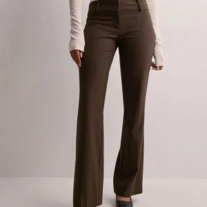 Kostymbyxor  - Jättesnygga bruna kostymbyxor med diskret randigt mönster och bootcutmodel. Byxorna har låg midja och klassisk dragkedja fram. Det är exakt samma byxor som på bilden och de är använda ett par enstaka gånger så nyskick!