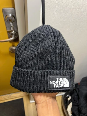 Svart ribbstickad mössa The North Face - Svart ribbstickad mössa från The North Face med uppvikt kant och tydlig logotyp framtill. Klassisk och enkel design som passar perfekt till kalla dagar. Tillverkad i mjukt material för extra komfort.