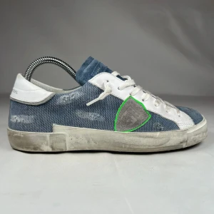 Philippe Model blå sneakers med mockadetaljer - Snygga blå sneakers från Philippe Model med vit snörning och vita detaljer. Ovandelen är i blått tyg med slitna effekter och inslag av mocka på tungan och tåpartiet. Sidan pryds av en grå mockasköld. Platt sula och rund tå för en chill vibe. Skoboxen ingår inte tyvärr.