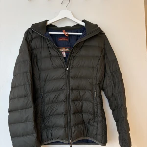 Grön dunjacka från Parajumpers  - Snygg mörkgrön dunjacka från Parajumpers i storlek L, men skulle säga är liten i storleken, mer en s/m. Jackan är quiltad, har huva och dragkedja framtill samt två sidofickor med dragkedja. Lättviktig och perfekt för kyliga dagar. Klassisk look med sportig känsla.