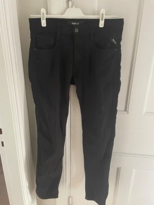 Svarta Replay Anbass jeans, storlek 32 - Säljer ett par svarta Replay Anbass jeans i storlek 32/32. De har en slim passform med klassisk femficksdesign och knappstängning. Materialet är mjukt och stretchigt för extra komfort. Snygga och stilrena jeans som funkar till det mesta.