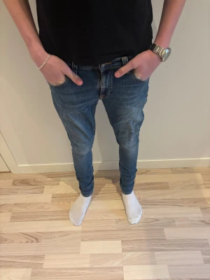  Nudie Jeans 28/34 - Snygga blå jeans från Nudie Jeans med klassisk orange söm och smal passform. Jeansen har fem fickor, normal midja och raka ben som smalnar av. Tillverkade i mjukt denimtyg som sitter skönt hela dagen.
